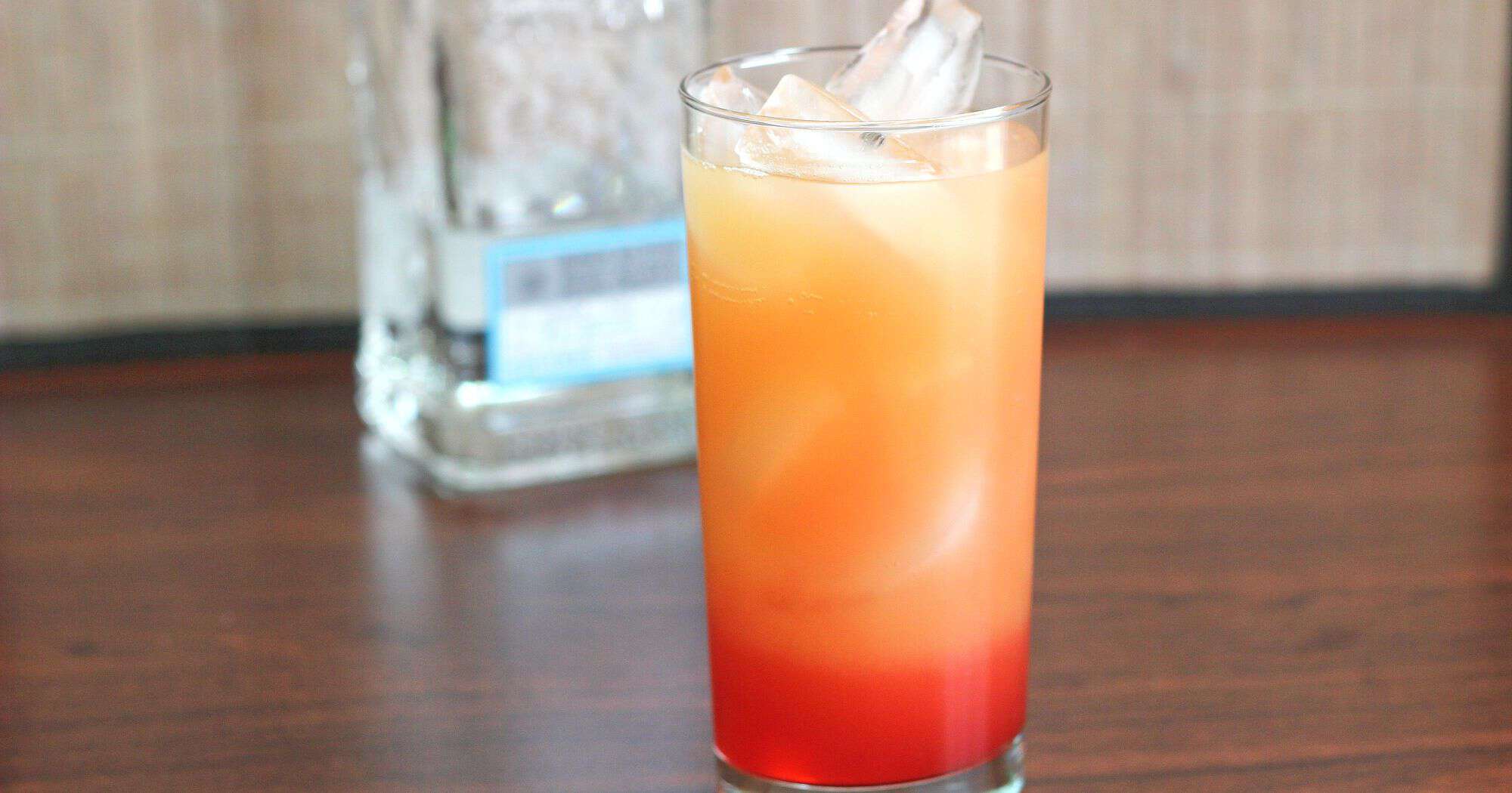 Tequila Sunrise drink on table in front of tequila bottle